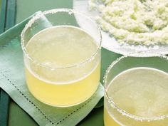 two glasses filled with yellow liquid sitting on top of a green napkin next to a white flower