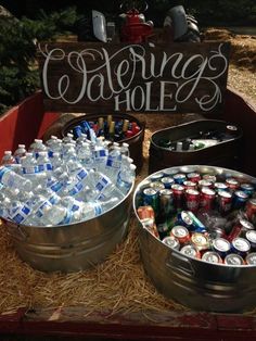 two metal buckets filled with water and soda bottles sitting on top of hay next to a sign