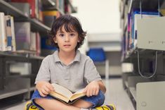 a young boy sitting on the floor reading a book