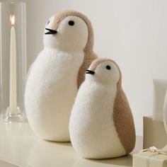 two stuffed penguins sitting on top of a table next to a gift box and candle