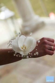 a person's hand holding a white flower with pearls and beads on the wrist