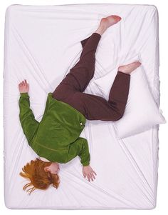 a woman laying on top of a bed under a white comforter with pillows next to her