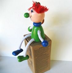 a toy sitting on top of a cardboard box with its legs spread out and red hair