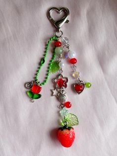 a keychain with charms attached to it on a white sheet that has a strawberry and other items hanging from it