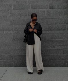 a woman standing in front of a brick wall looking at her cell phone