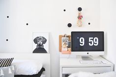 a white desk topped with a computer monitor next to a wall covered in black polka dots