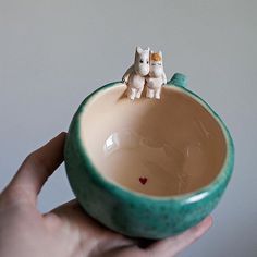 a hand holding a small ceramic bowl with two cats on the top and a heart in the middle