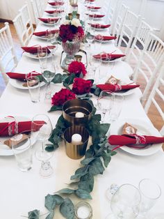 the table is set with white chairs and red napkins, silverware and flowers