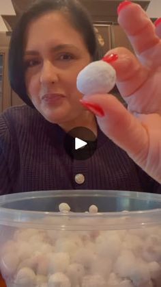 a woman holding up a small white ball in front of a container filled with cotton balls