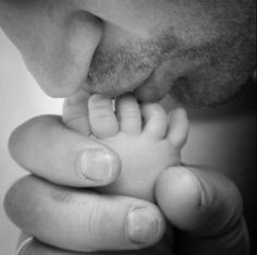 a black and white photo of a man holding a baby's hand