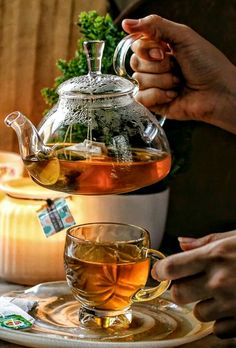 a person pouring tea into a glass teapot on top of a white saucer