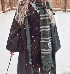 a woman standing in the snow with a scarf around her neck and holding ski poles