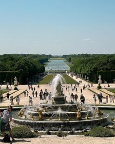 a large fountain in the middle of a park with lots of people walking around it