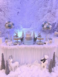 a table topped with cakes and animals next to snow covered trees in front of a snowy mountain