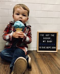 a little boy sitting on the floor eating an ice cream cone with a sign saying i've got the scoop my baby brother is due sep 2013