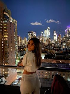 a woman standing on top of a building next to a cityscape at night