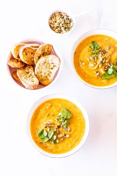 three bowls filled with soup next to some bread