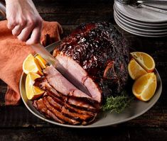 a person cutting up a ham on a plate with oranges and lemons next to it