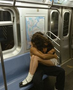 two people sitting on a subway train with their arms around each other's shoulders