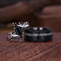 two wedding rings with black diamonds on them sitting on top of a wooden table next to each other