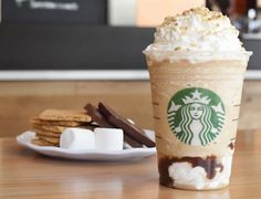 a starbucks drink with marshmallows and chocolate on the side sitting on a table