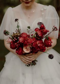 a woman in a white dress holding a bouquet of red and pink flowers on her wedding day