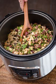 a person stirring food in a crock pot with a wooden spoon on the side