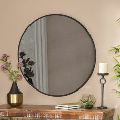 a round mirror sitting on top of a wooden table next to a vase with flowers