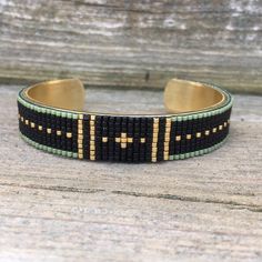 a black and green bracelet with gold crosses on it, sitting on a wooden surface