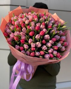 a person holding a bouquet of tulips with purple ribbons on the ends and pink flowers in the middle