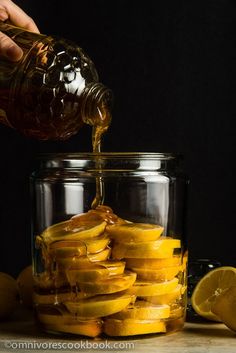 someone pouring honey into a glass jar filled with sliced lemons