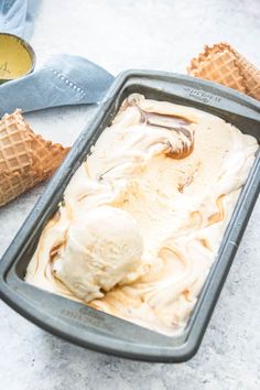 two scoops of ice cream sitting in a pan next to some cones on the table