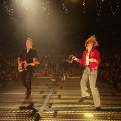 two people on stage playing guitars and singing in front of an audience at a concert