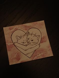 a drawing of two cats hugging in front of a heart on a piece of paper