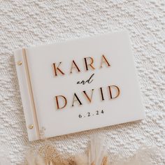 a wedding guest book laying on top of a white blanket with gold lettering and feathers