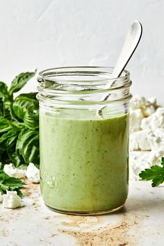 a jar filled with green smoothie next to fresh basil leaves and feta cheese