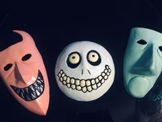 three masks with faces painted on them sitting next to each other in front of a black background