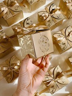 a hand is holding up a gold gift box in front of many golden boxes with bows on them