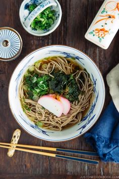 a bowl of noodles and vegetables with chopsticks next to it on a wooden table