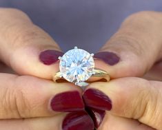 a woman's hands holding a ring with a white diamond in it and red nail polish