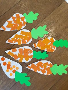 paper cut out carrots sitting on top of a wooden table with green and orange dots