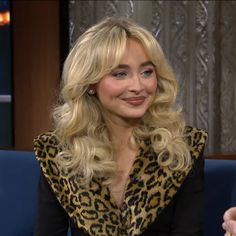 a woman with long blonde hair sitting on a blue couch and smiling at the camera