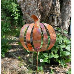 a metal pumpkin sitting on top of a wooden pole next to a lush green forest