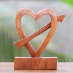 a wooden heart shaped sculpture with an arrow sticking out of it's center, sitting on a table