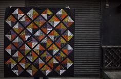 a person holding up a large quilt on the street in front of a garage door