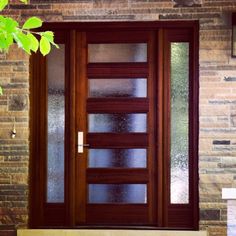 the front door is made of wood and has glass panels on each side, along with a brick wall