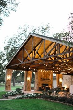 a covered patio with string lights on the roof and tables in the grass below it