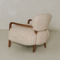 a chair made out of sheep's wool with wooden legs and back rests against a white wall