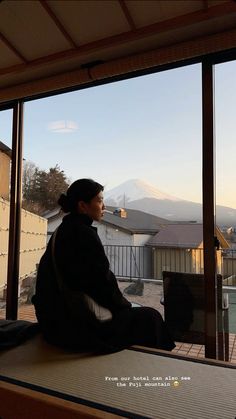 a woman sitting on top of a window sill looking out at the snow covered mountains