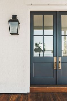 a blue front door with a white brick wall and two black lanterns on the side